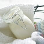 White homeamde moisturizing lotion in a jar on a bed of white towels in a basket.