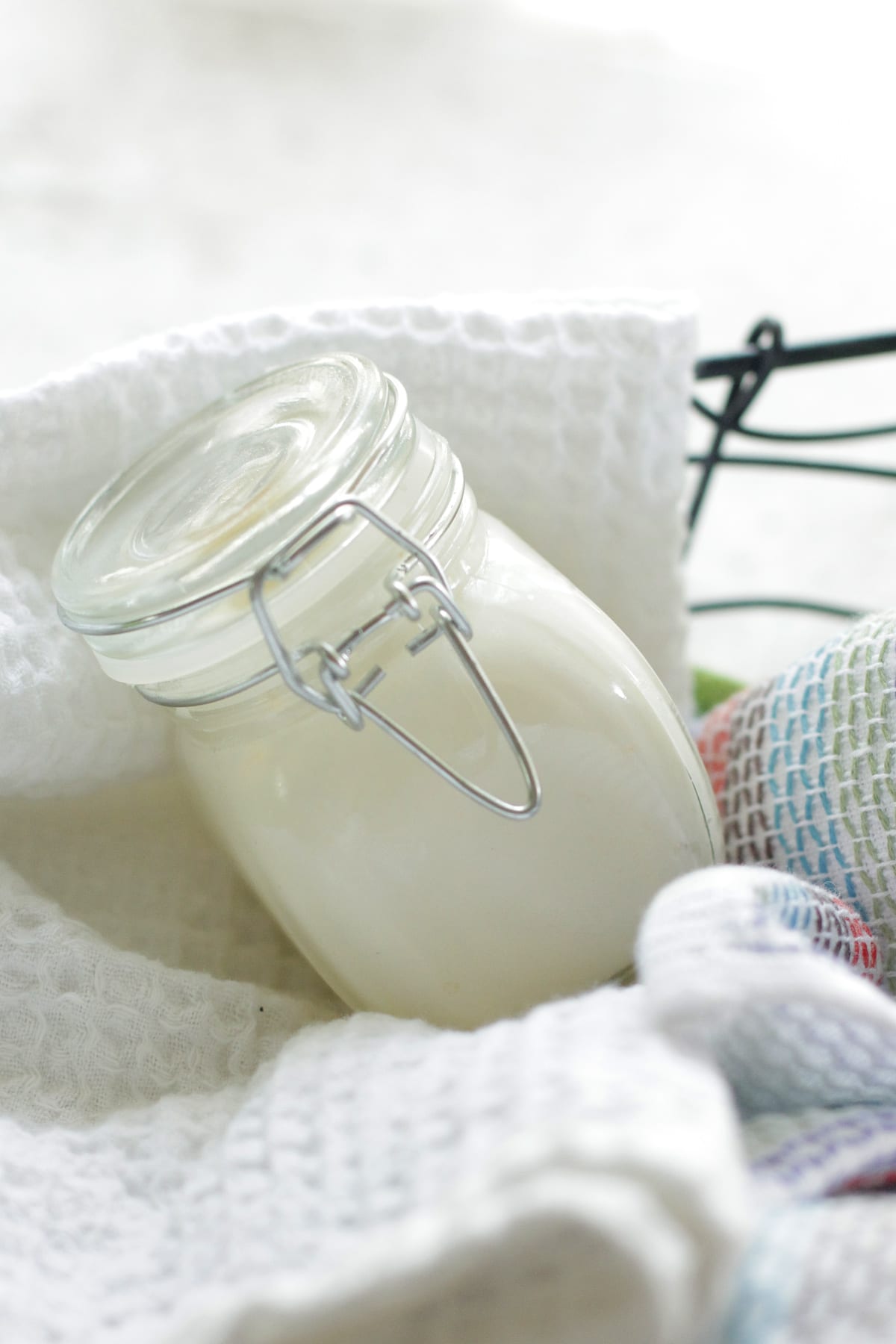 White homeamde moisturizing lotion in a jar on a bed of white towels in a basket.