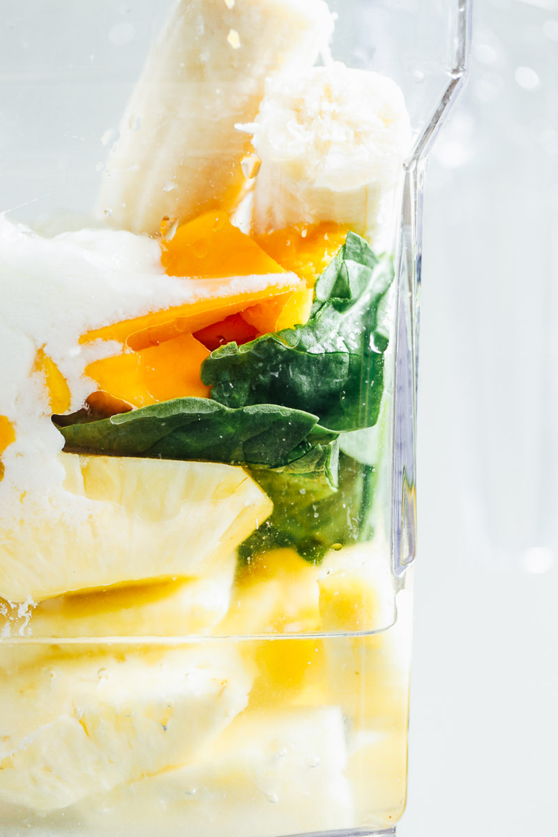 Smoothie ingredients in a blender: pineapple, mango, yogurt, banana, spinach.
