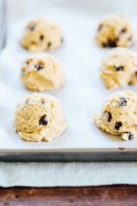 Mounds of chocolate chip cookie dough on a sheet pan lined with parchment paper.