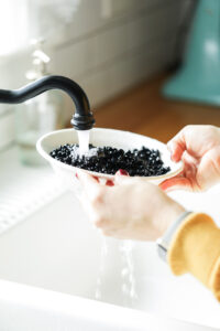 Rinsing off dry black beans off in a colander at the sink with running water.