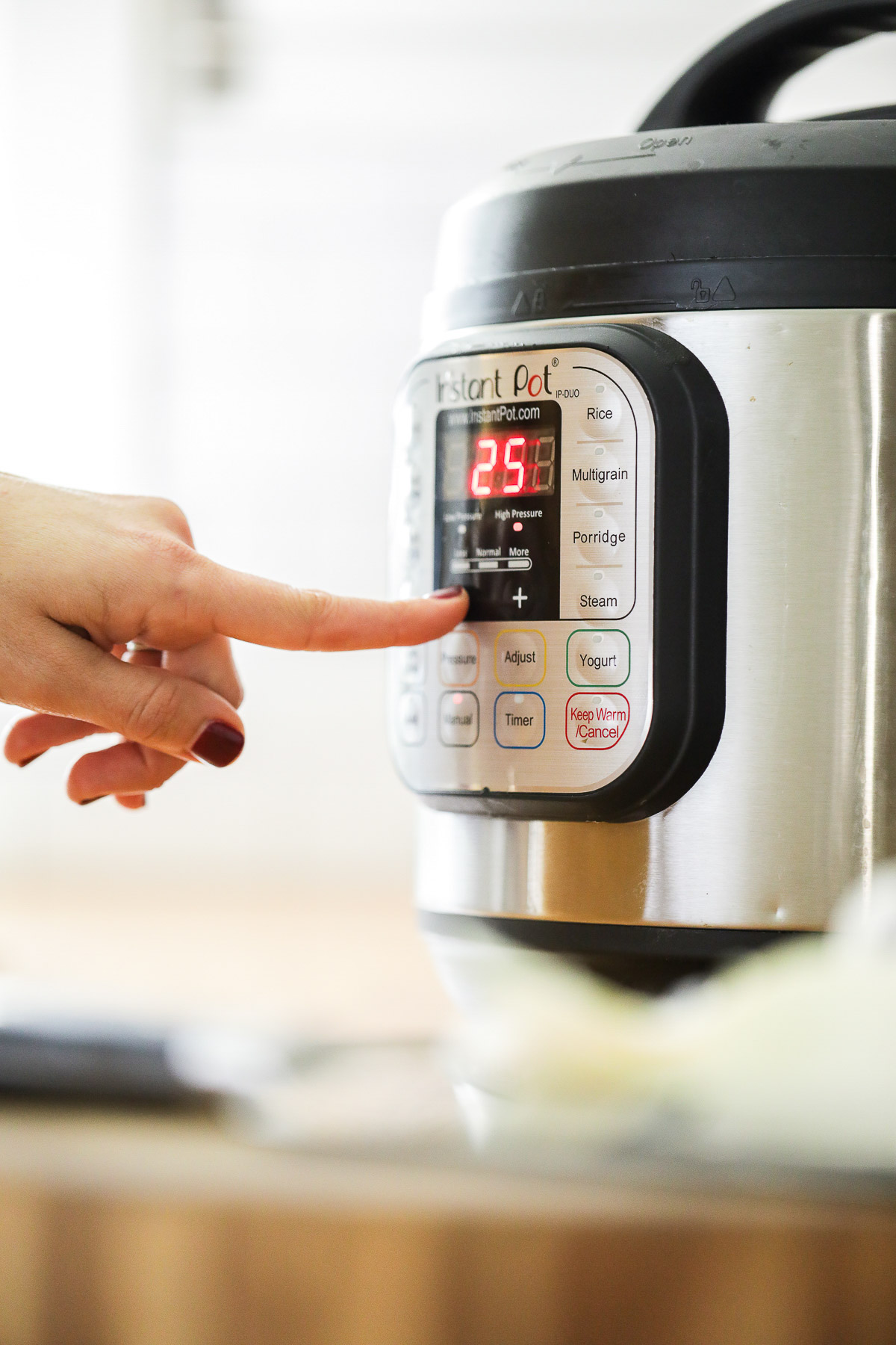 A finger pressing the pressure cook setting on the front of the Instant Pot.