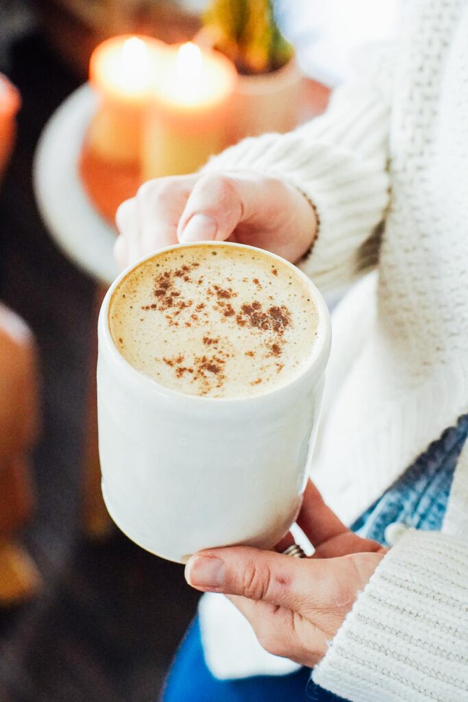 Hands holding a pumpkin spice latte in a white mug.