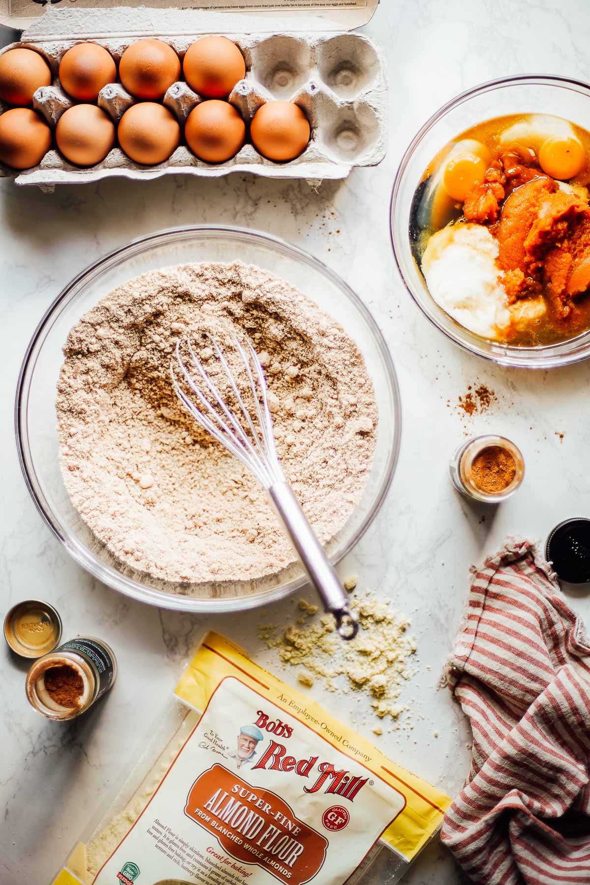 Almond flour in a clear glass bowl with a whisk and pumpkin puree, maple syrup, and yogurt combined in a separate bowl.