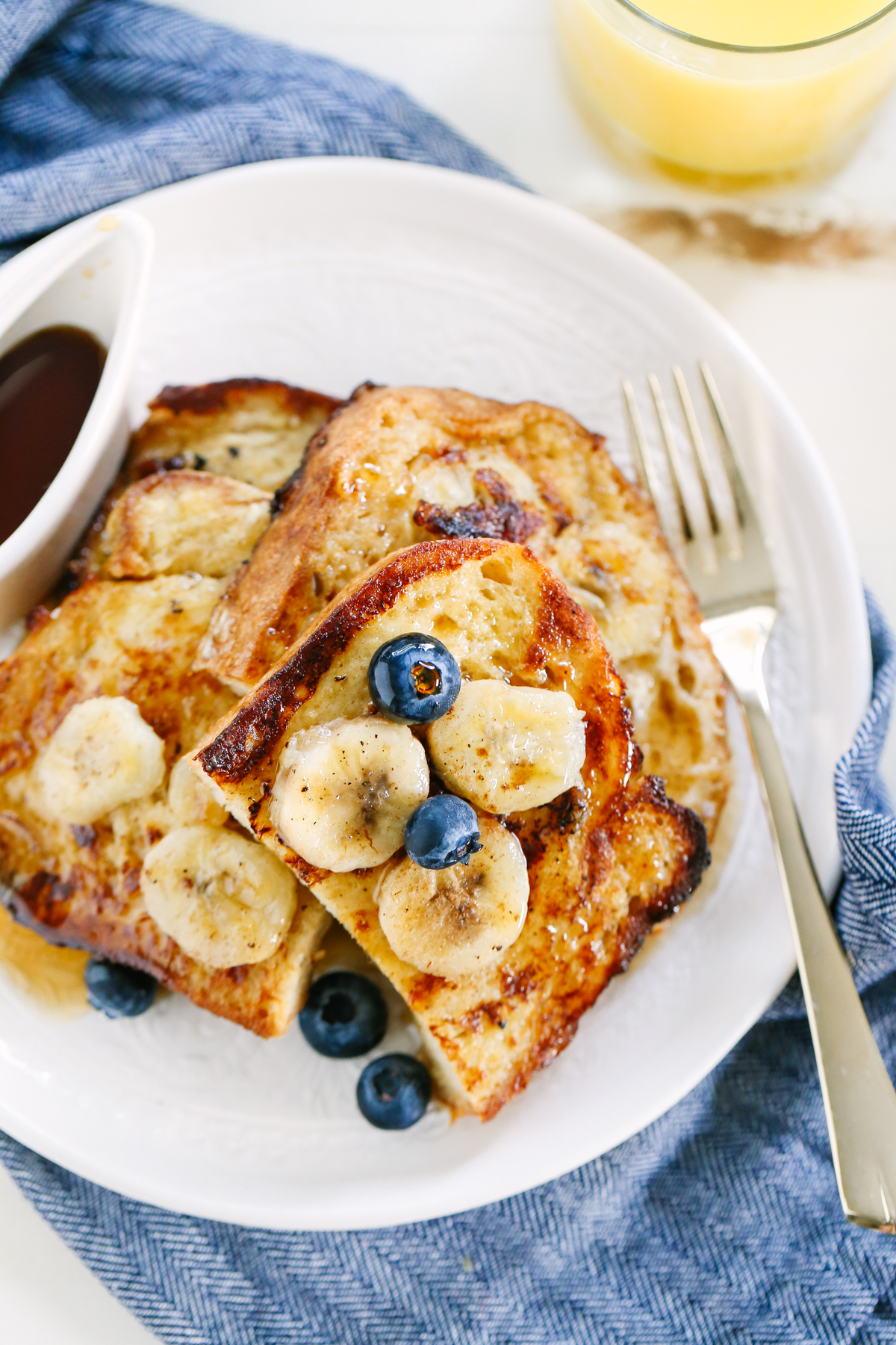 French toast slices on a white plate with blueberries and bananas on top.
