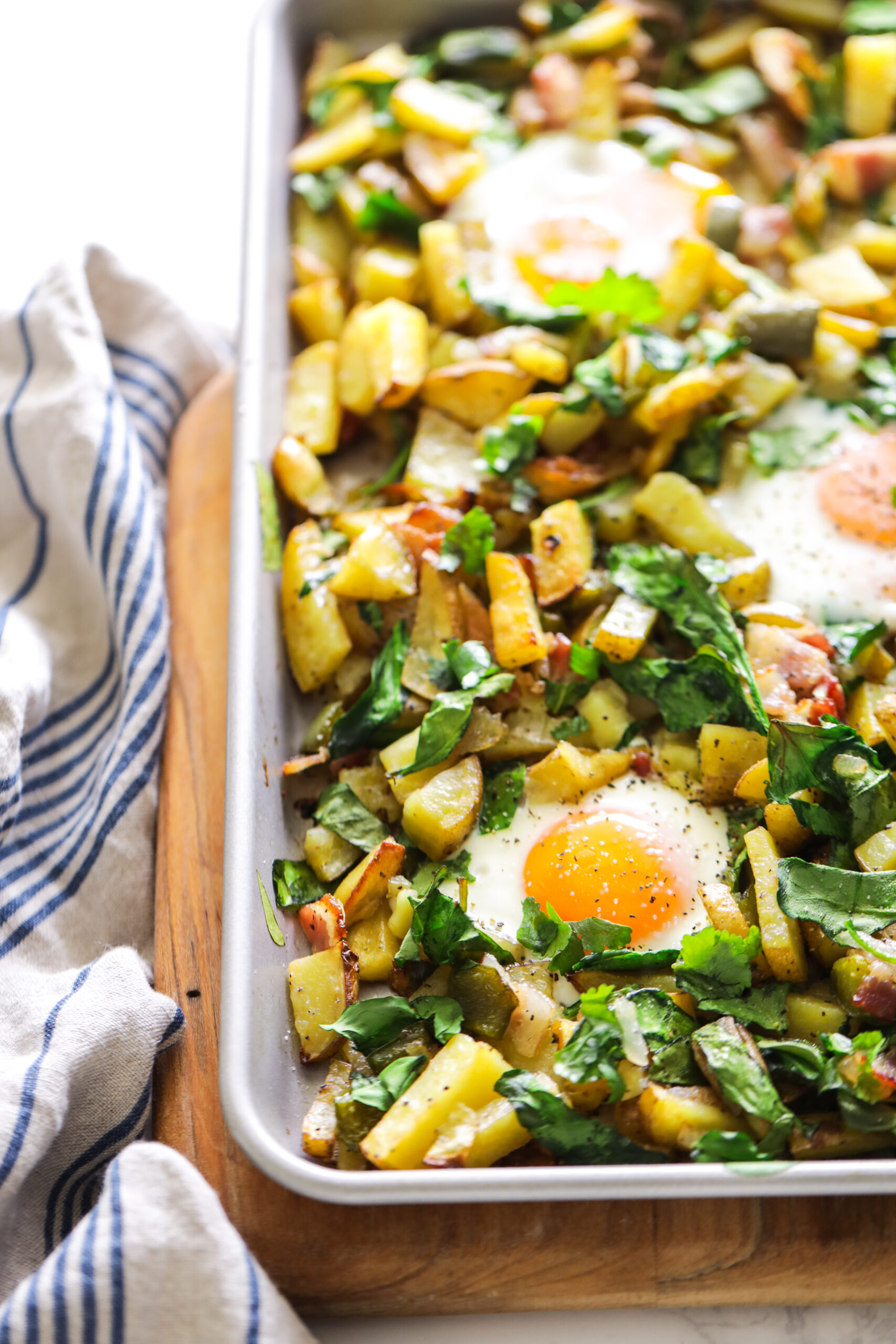 Potatoes, bacon, spinach, and eggs cooked on a sheet pan.