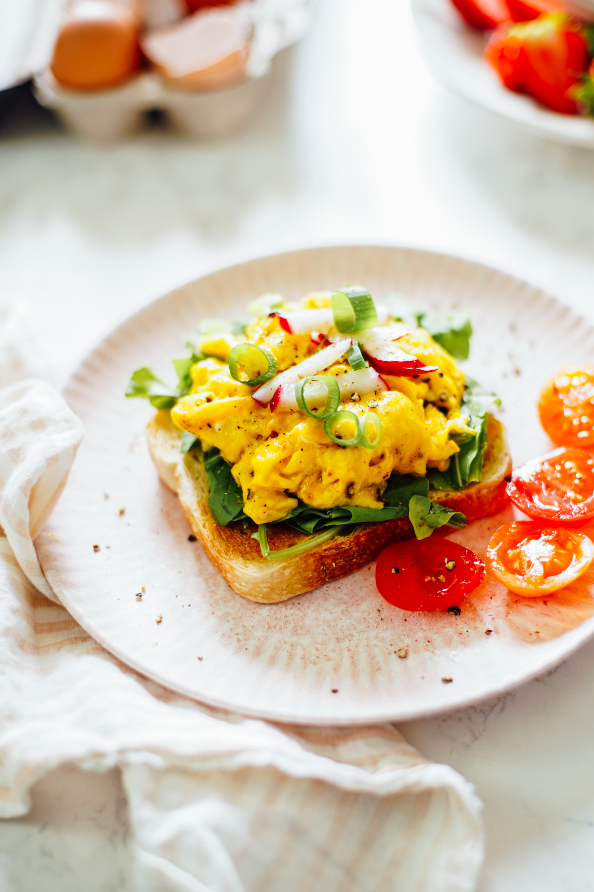 Breakfast sandwich: scrambled eggs on a slice of toast with arugula and radish slices on a pink plate.