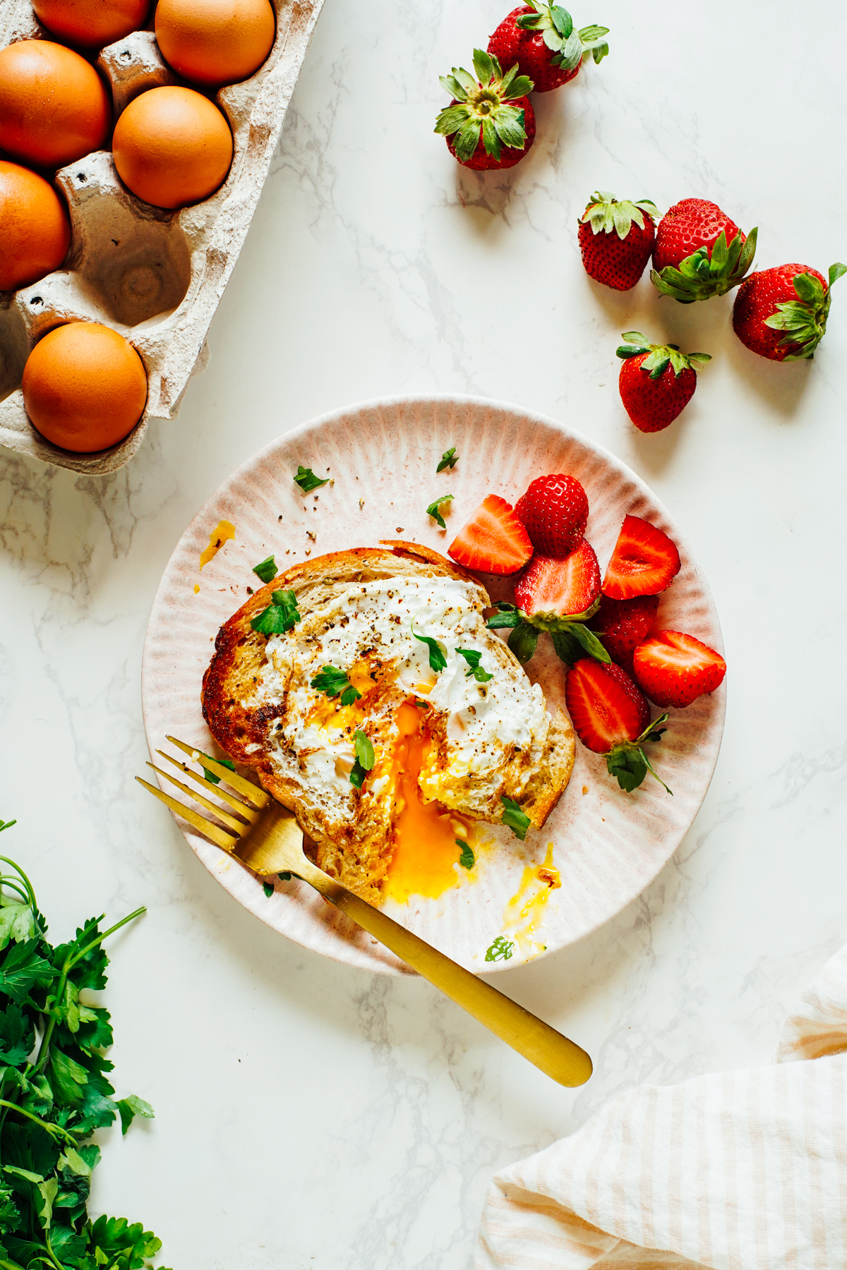 Eggs in a Basket cut with a fork on a pink plate with strawberries.