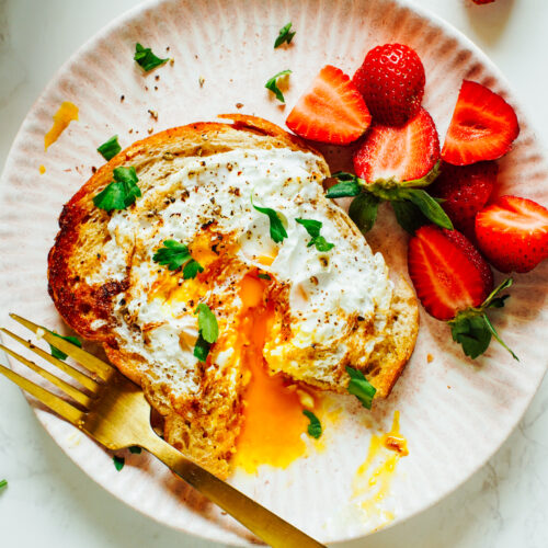 Eggs in a Basket cut with a fork on a pink plate with strawberries.