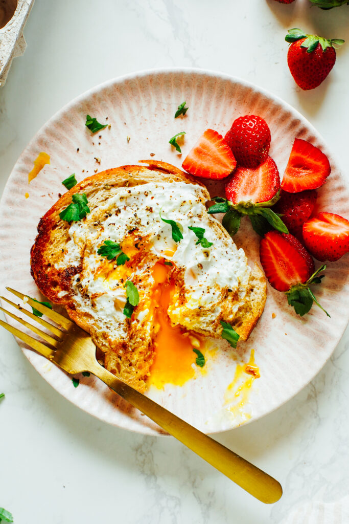 Eggs in a Basket cut with a fork on a pink plate with strawberries.