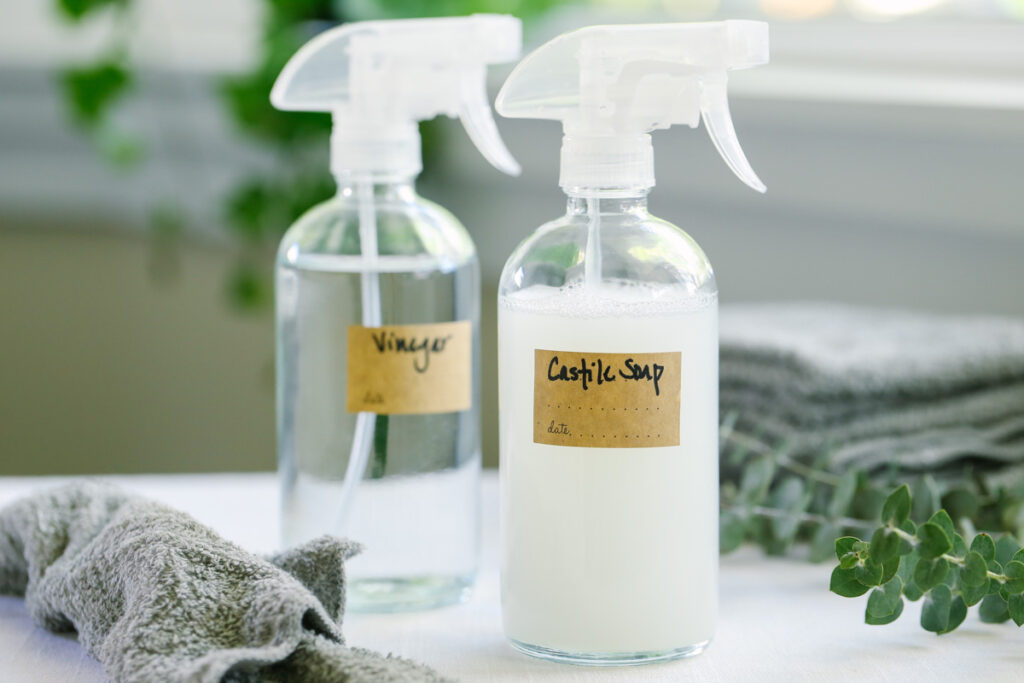 Castile Soap all-purpose cleaner in a glass spray bottle with vinegar cleaner in the back.