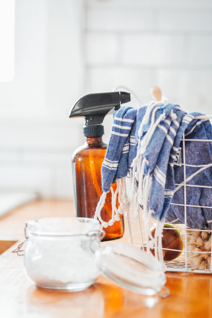 Glass spray bottle filled with all purpose cleaner hanging off a basket in the kitchen.