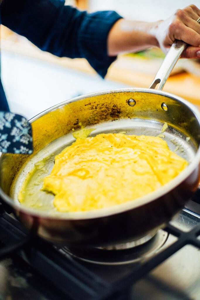 Tilting a skillet with whisked eggs cooking inside.