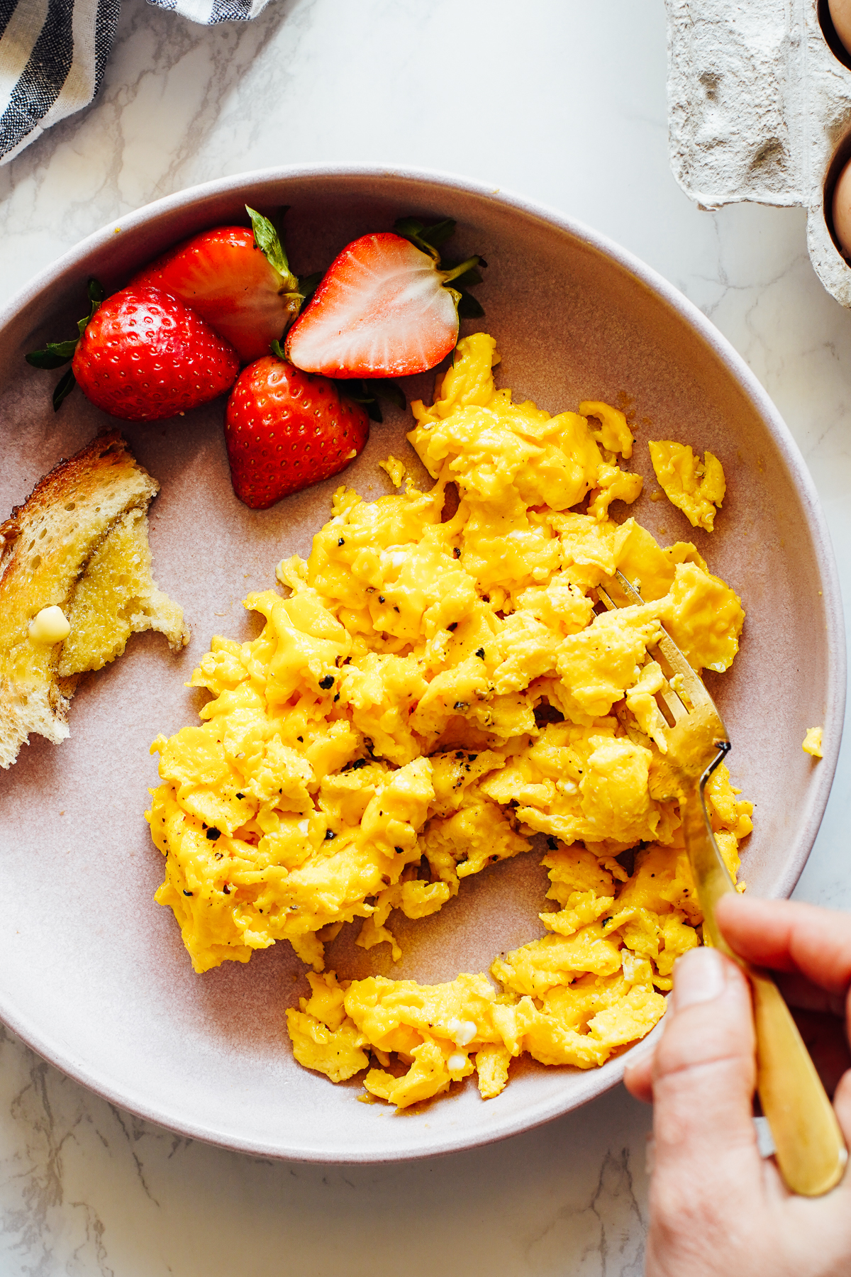 Soft scrambled eggs on a pink plate with strawberries.