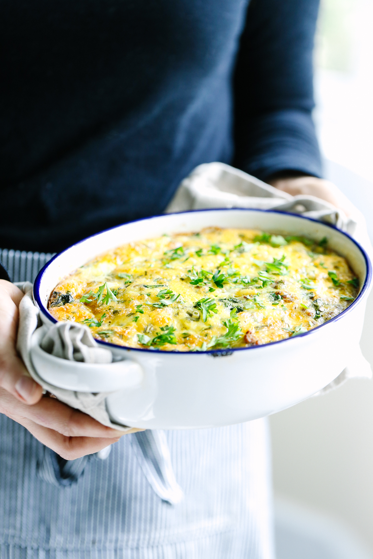 Hands holding a casserole dish with baked egg casserole inside.