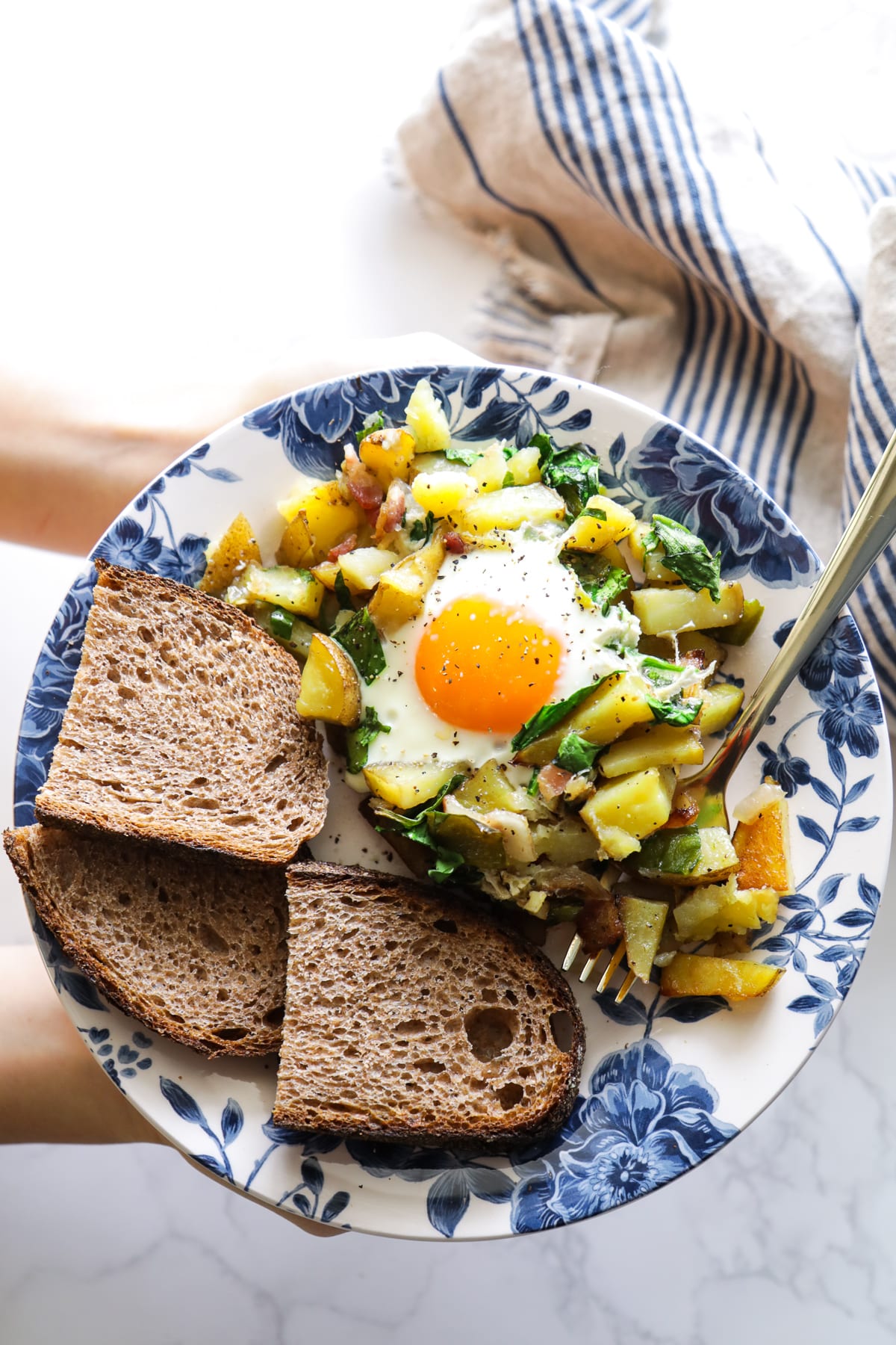 Egg (sunny side up) and potato hash with toast on the side on a blue and white floral plate.