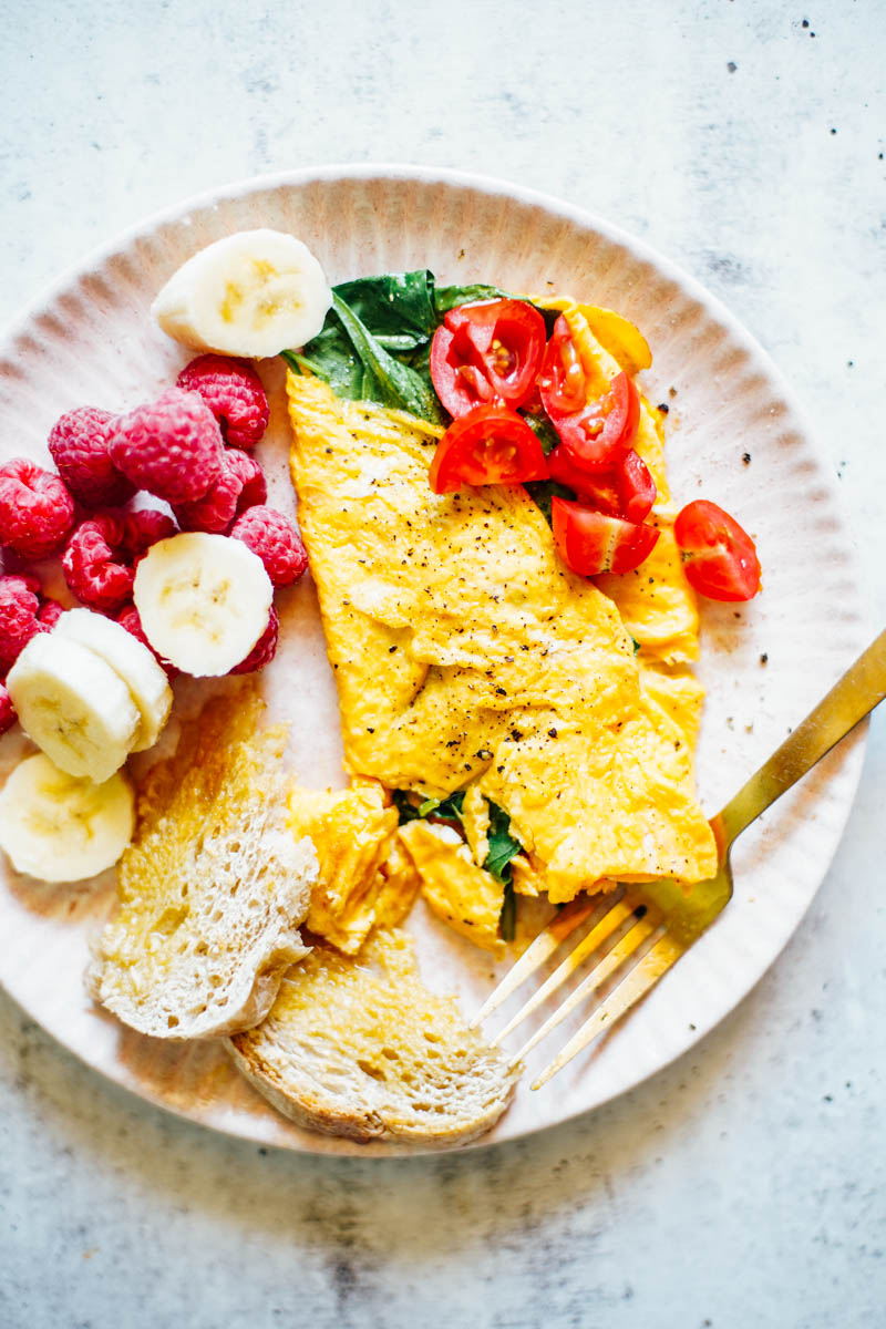 Spinach omelette with tomatoes and raspberries and bananas on the side.