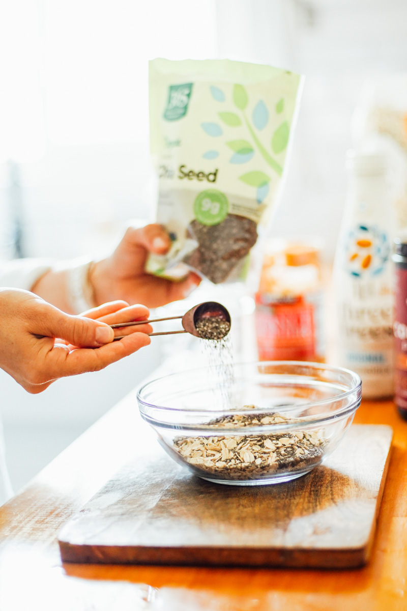 Adding chia seeds to a glass bowl with oats inside.