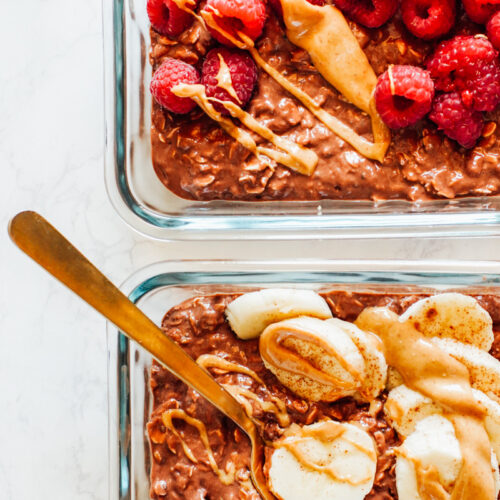 Chocolate peanut butter overnight oats in meal prep glass jars topped with banana and raspberries.