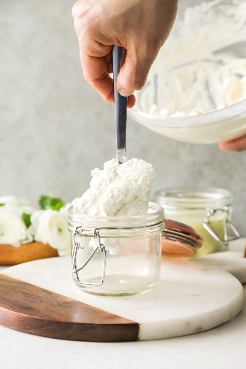 Spooning lotion into a glass jar.