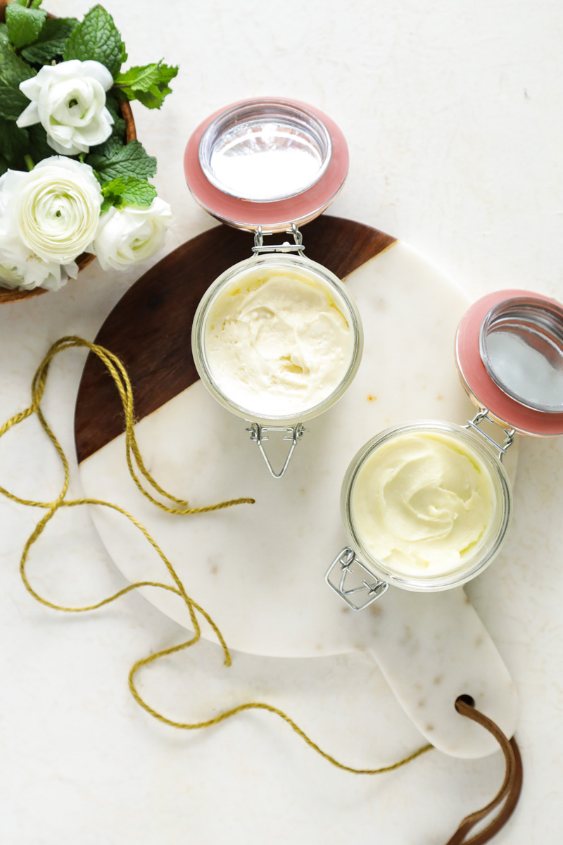 Lotion in glass jars on a cutting board.