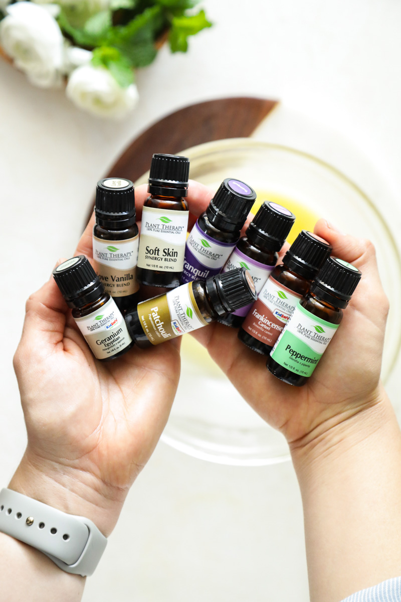 Essential oils being held in the palm of a hand over a jar of lotion.