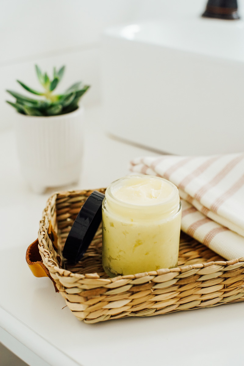 Homemade shea butter lotion in a clear glass jar on a bathroom counter.