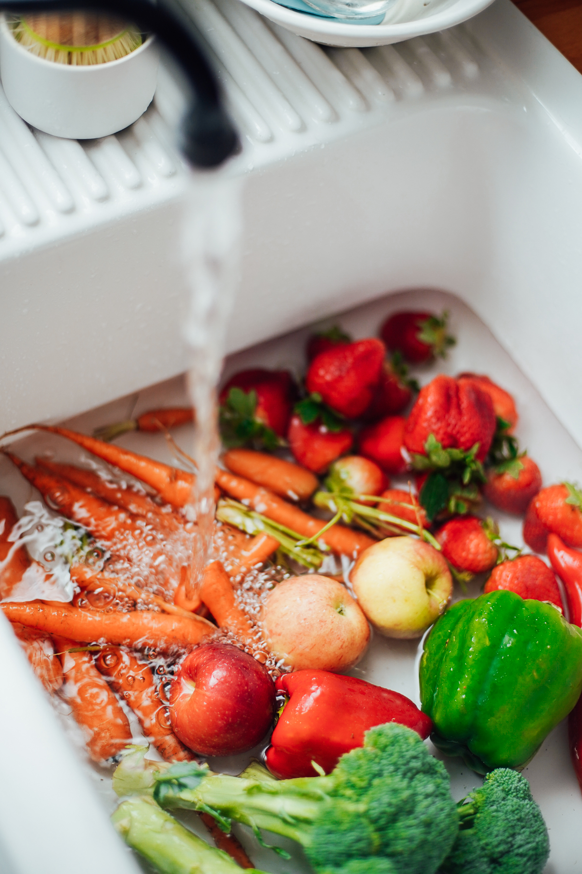 Fruits and vegetables in a sink being filled with water for a homemade produce wash.