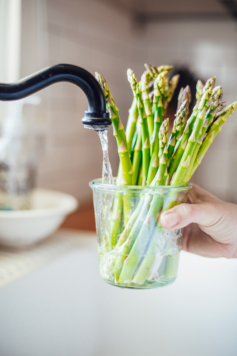 Filling the glass jar with asparagus inside with fresh water at the sink.