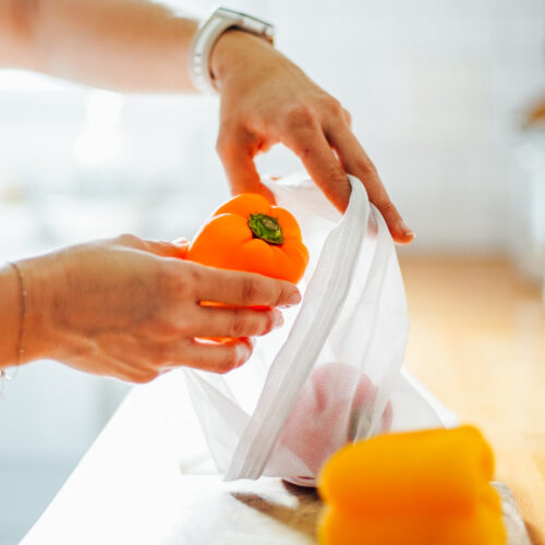 Placing an orange bell pepper in a reusable bag.