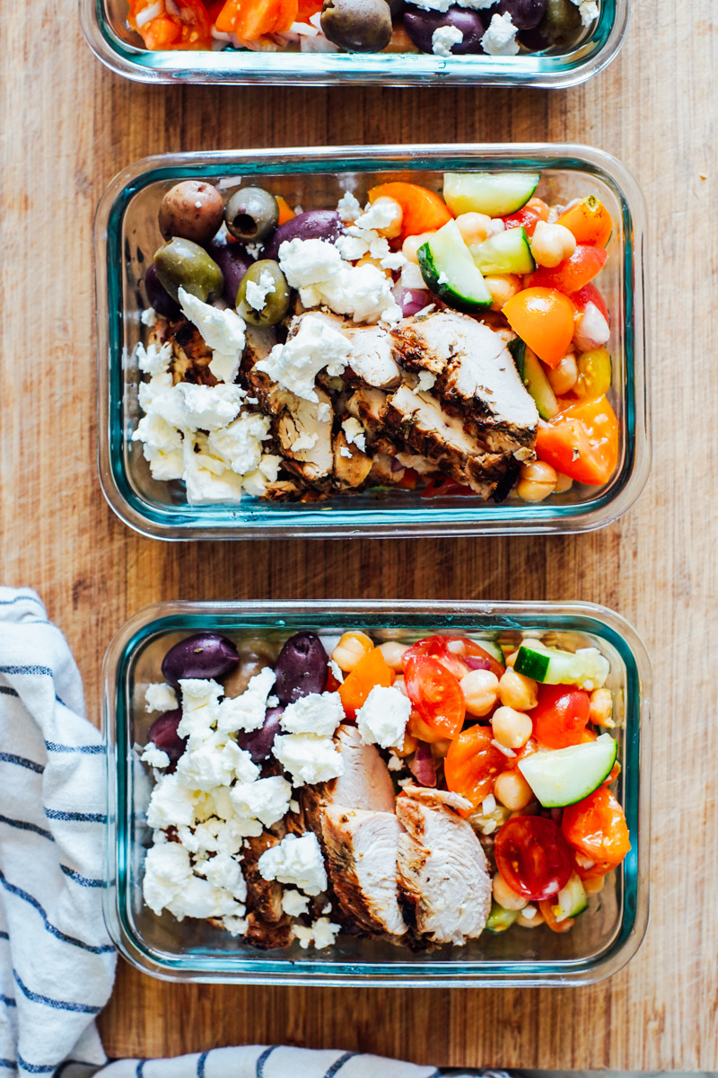 Meal prep chicken bowls in glass containers lined up on a cutting board.