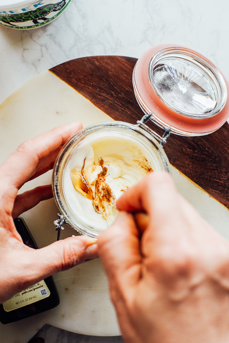 Stirring honey and cinnamon into the yogurt in a glass bowl.