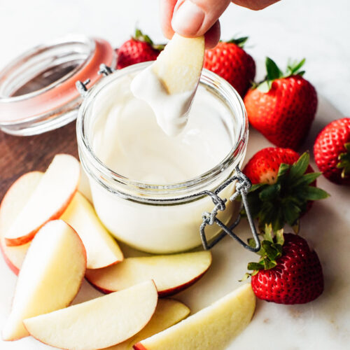 Yogurt fruit dip in a glass bowl with strawberries and apples on the side.