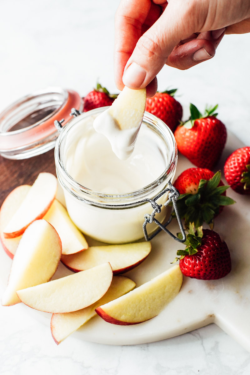 Yogurt fruit dip in a glass bowl with strawberries and apples on the side.