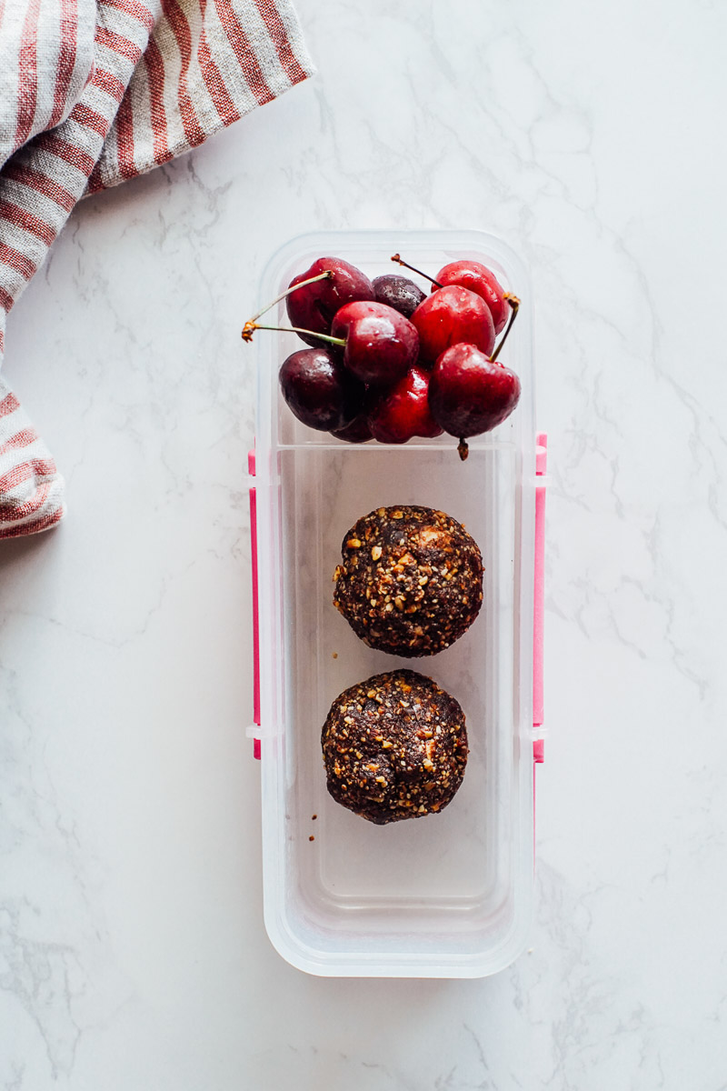 Fruit and nut bites (homemade Lara bars) in a plastic snack container with cherries.