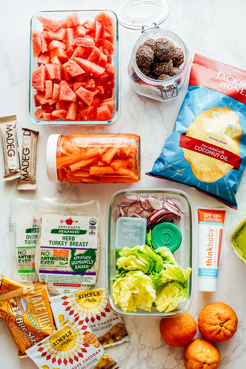 Summer snacks laid out on a counter. Fresh fruit, chips, granola bars, energy bites.