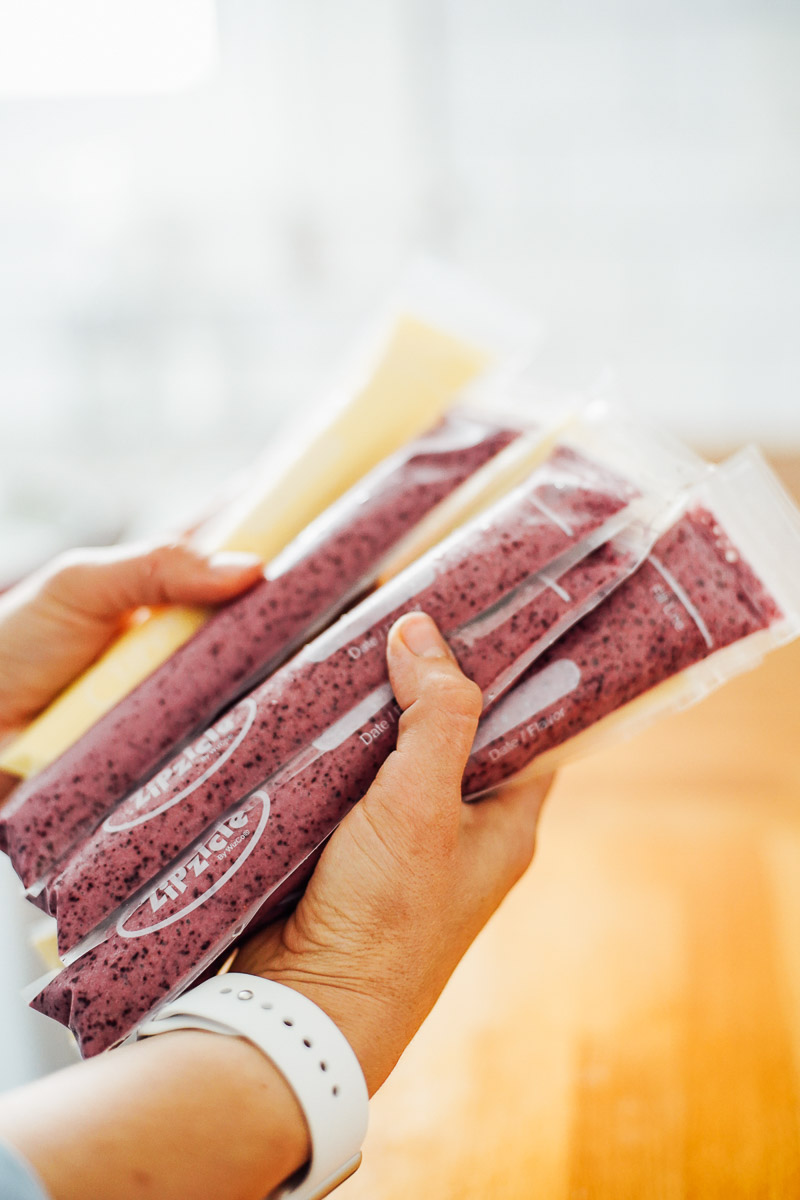 Homemade yogurt sticks being held on a counter: yogurt, honey, fruit in plastic pouches.