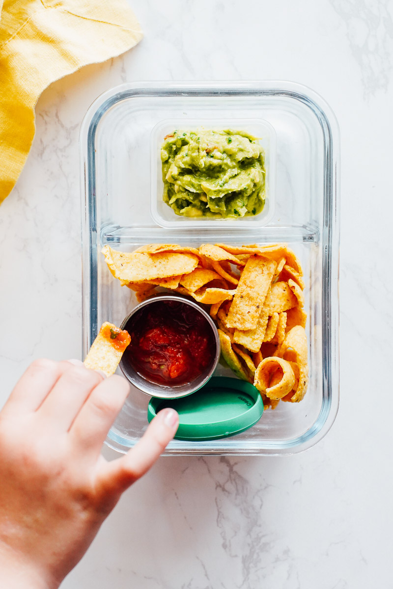 Corn chips with salsa and guacamole in a glass snack container.