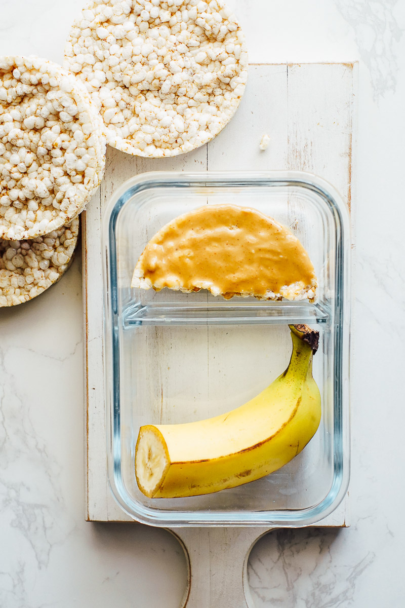 Banana, rice cake, and peanut butter on the rice cake in a glass container.