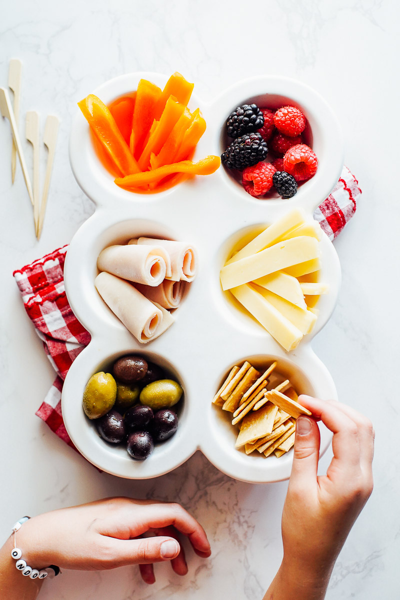 Snack board with carrots, turkey, cheese, fruit, olives, and carrots in a muffin tray.