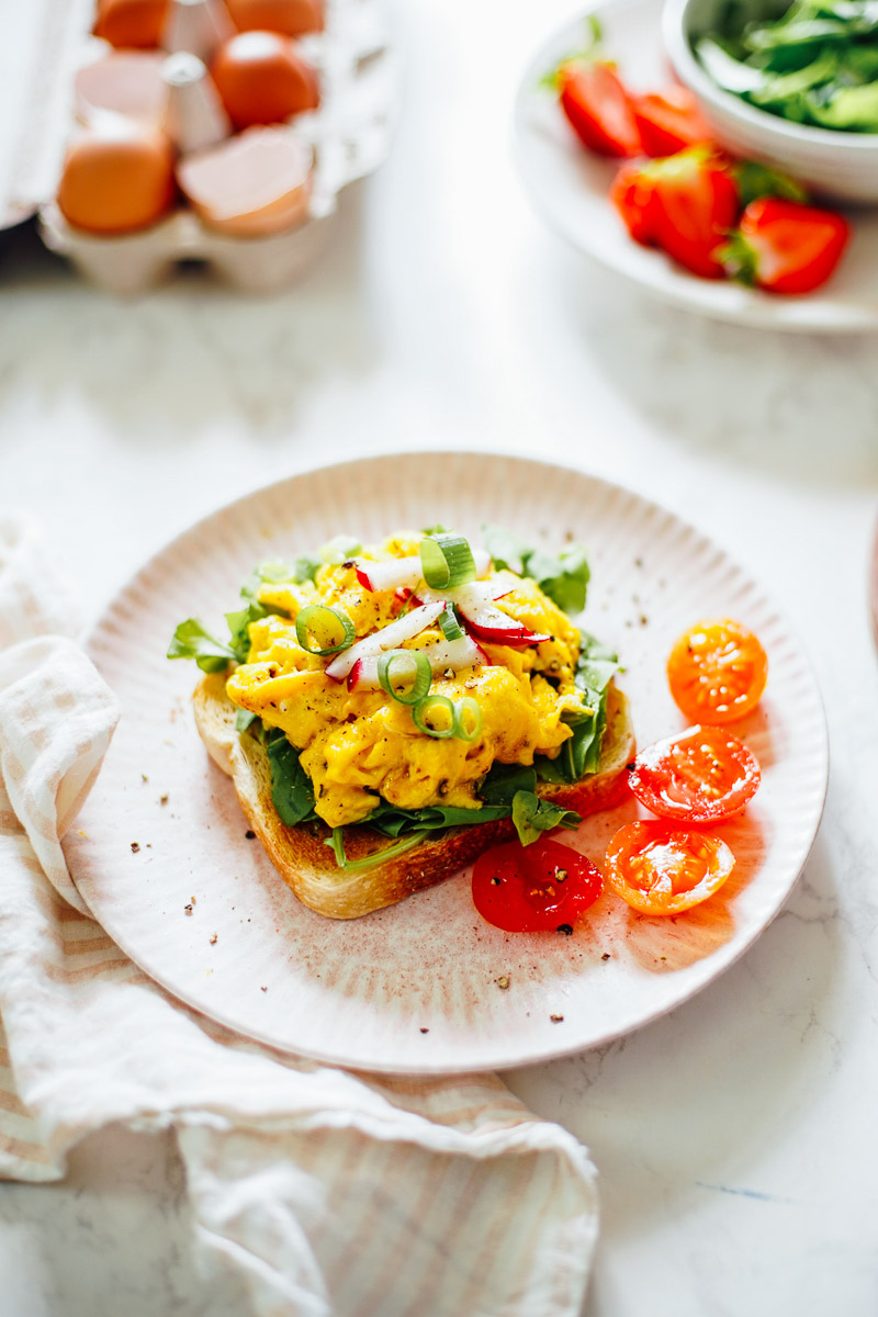 Scrambled eggs on toast with arugula and tomatoes.