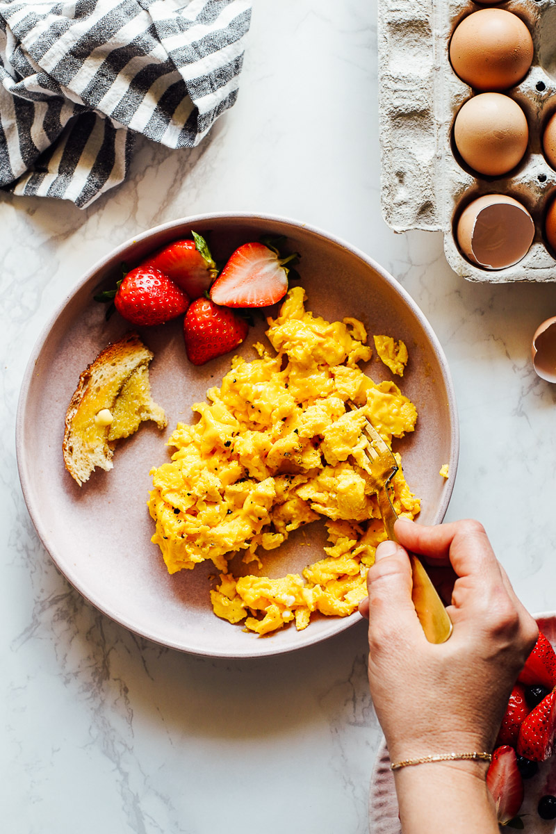 Scrambled eggs on a pink plate with strawberries.