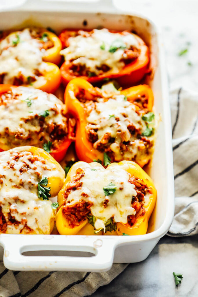 Stuffed bell peppers covered in cheese in a white ceramic baking dish.