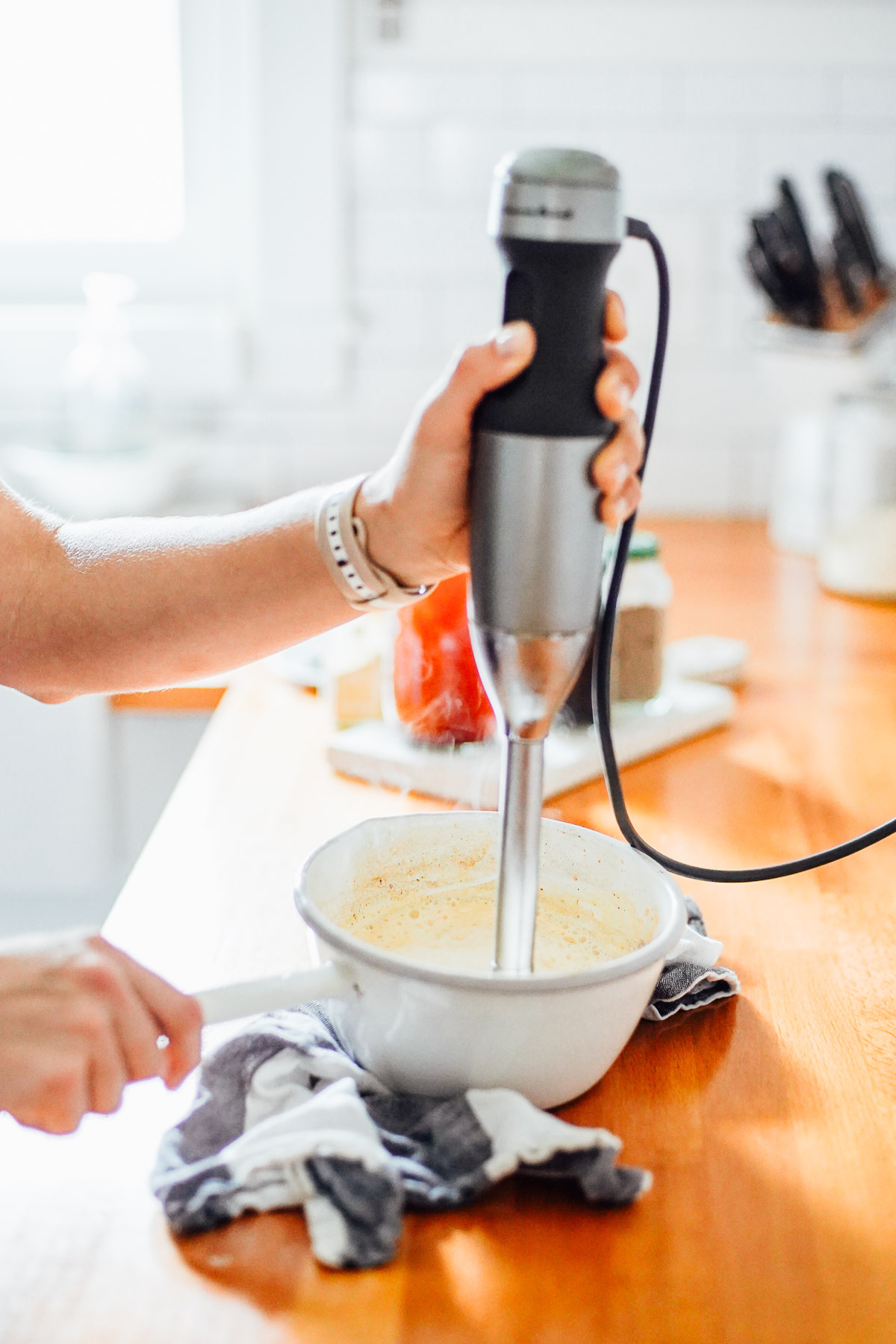 Using an immersion blender to froth milk in a white ceramic pot.
