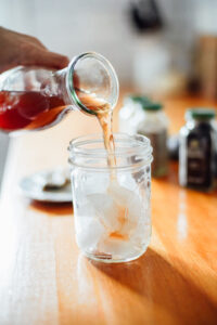 Pouring chai concentrate into a mason jar filled with ice cubes.