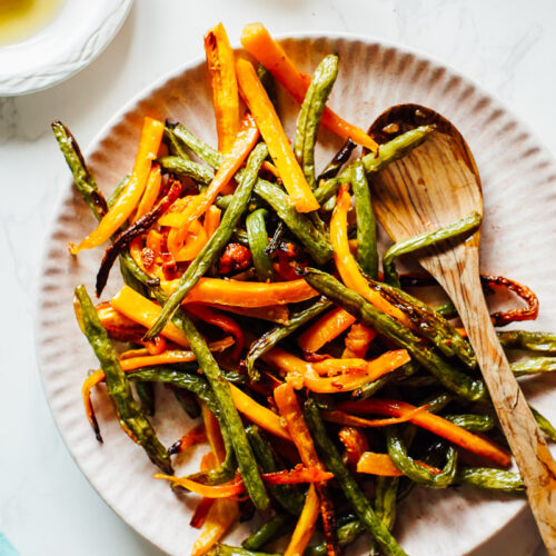 Roasted carrots and green beans on a pink serving plate.