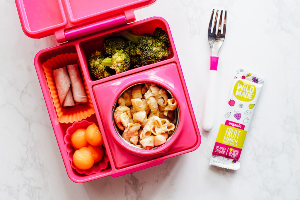 Macaroni and cheese in a thermos with cantaloupe, rolled up ham, and broccoli in a lunchbox.