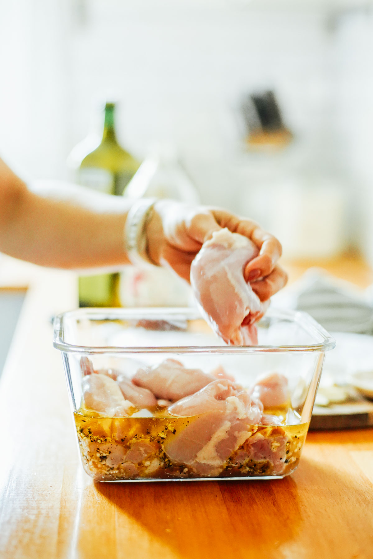 Adding chicken thighs to the marinade in a large glass bowl.