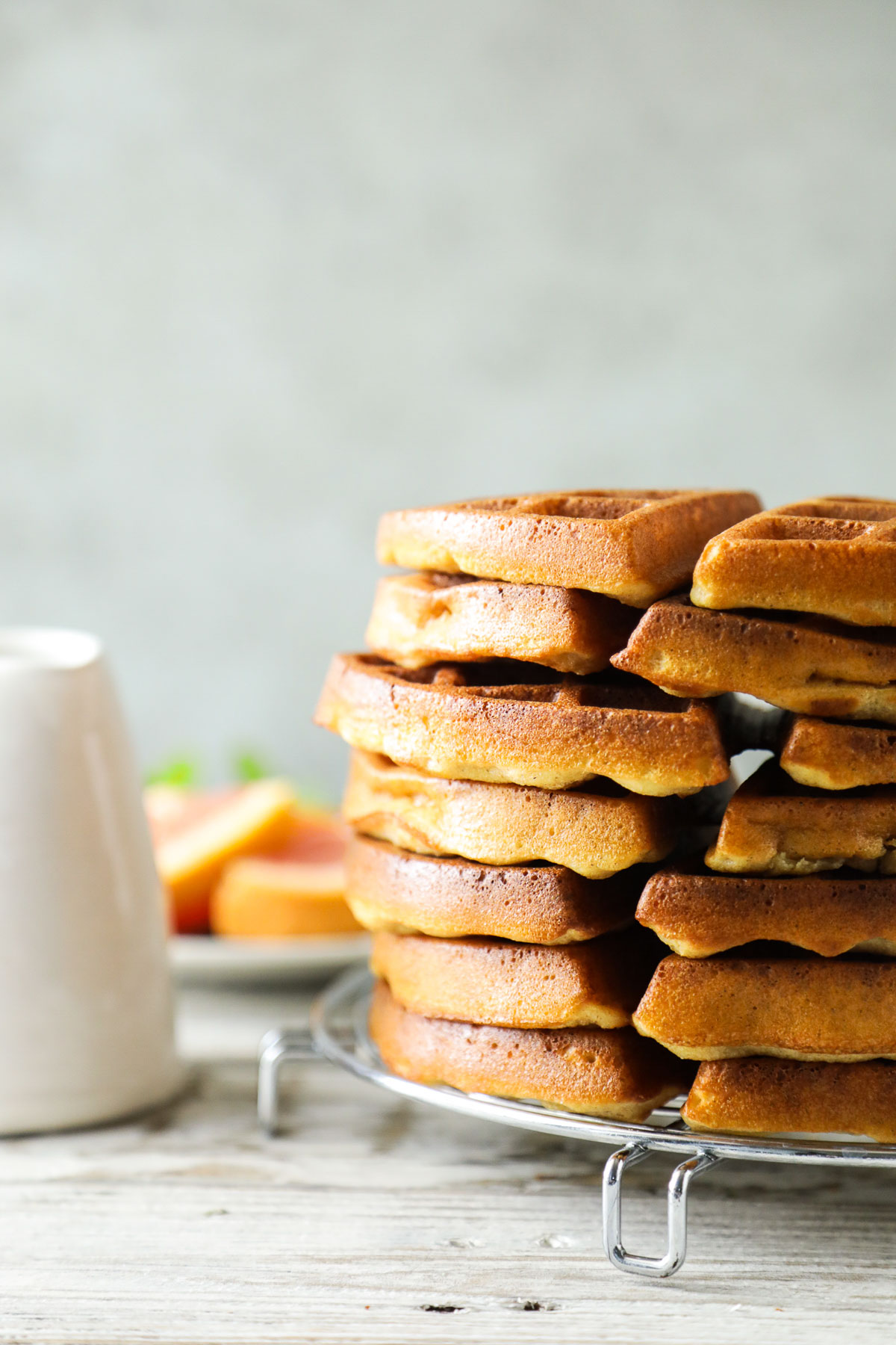 Waffles stacked on a cooling rack with maple syrup in the background.