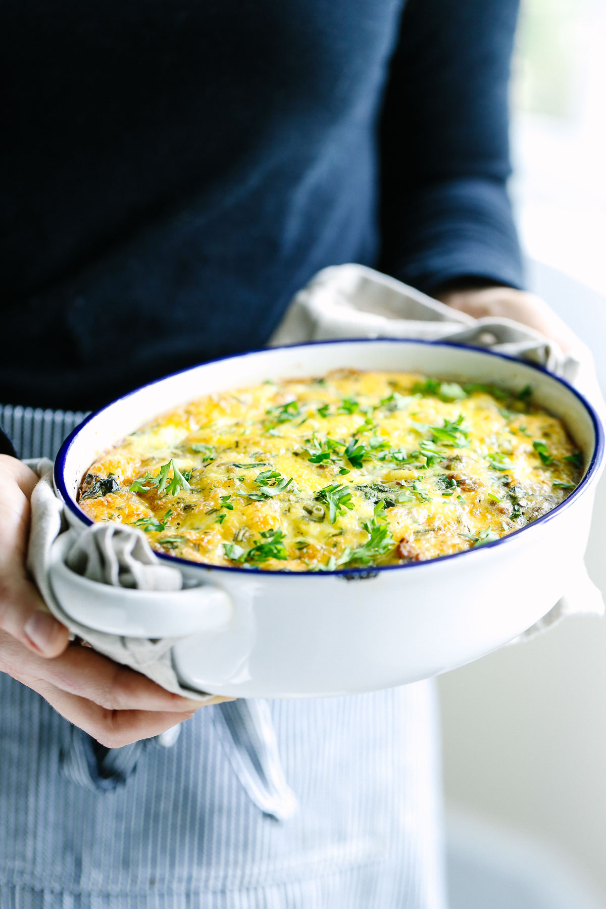 Hands holding a breakfast casserole baked in a casserole dish.